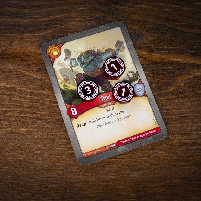 Primary Set Damage tokens on the Troll card from Keyforge, one token is on its three-damage side and two tokens are on their one-damage side.