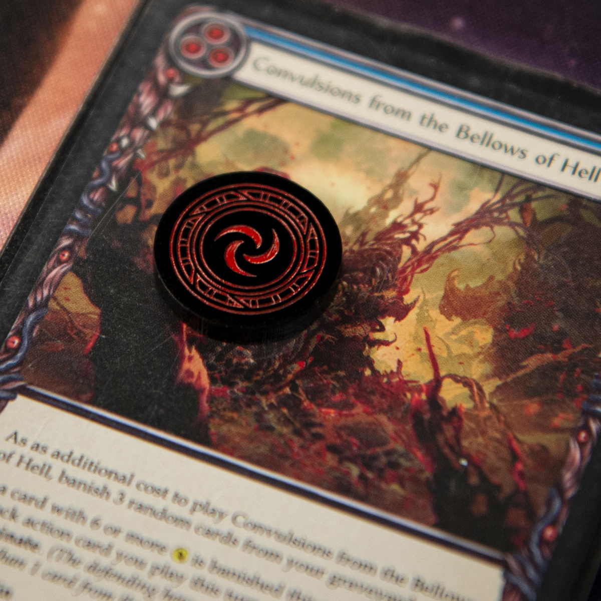 Close up of a single Resource Token on top of the Flesh and Blood TCG card, Convulsions from the Bellows of Hell (Blue)