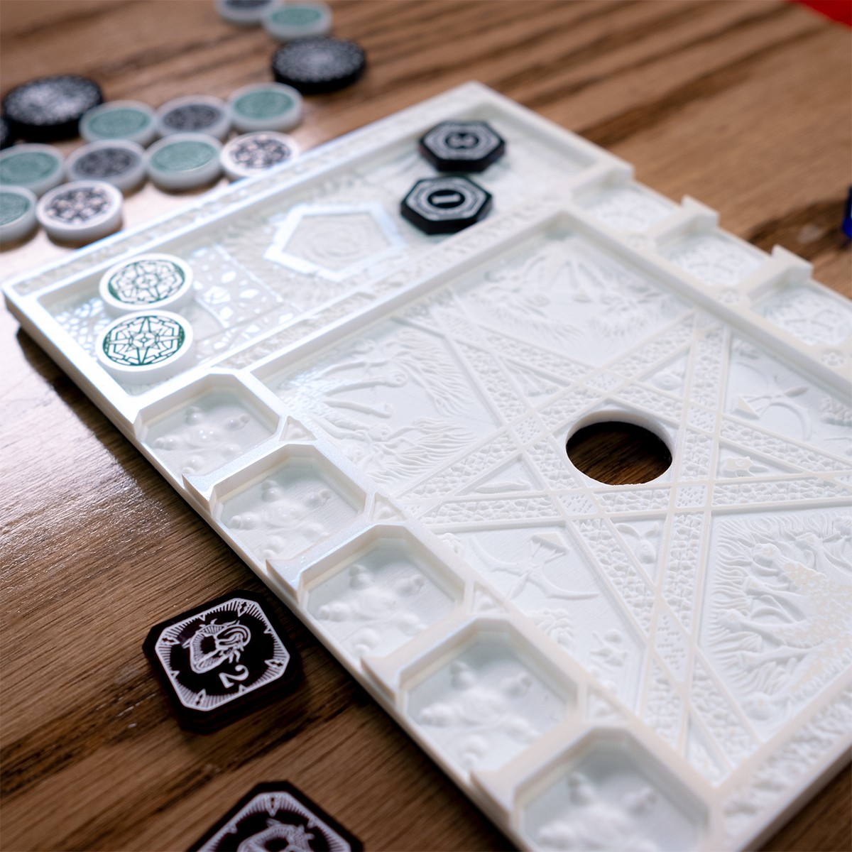 Close up of the Edge of the Earth Mythos Board highlighting the eldritch cartouches and reliefs of the Elder Things the comprise the design of the card holder section.  At the top of the frame, the Mythos Board glows in the light