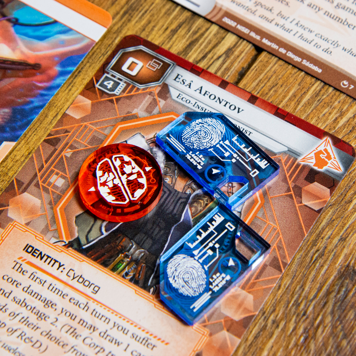 A Brain Damage Token and two Tag Tokens from the Data Token set on top of the Null Signal Games Netrunner card, Esâ Afontov