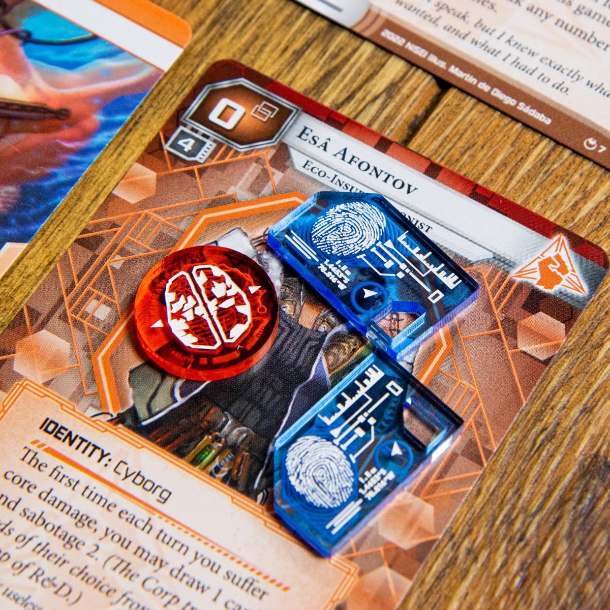 A Brain Damage Token and two Tag Tokens from the Data Token set on top of the Null Signal Games Netrunner card, Esâ Afontov