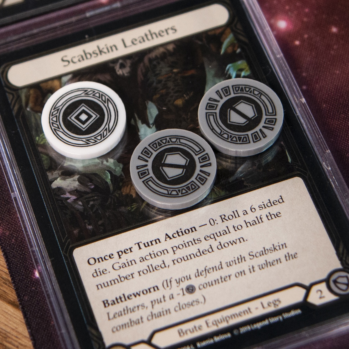 One Activation Token and two Armor Tokens on top of the Flesh and Blood TCG card, Scabskin Leathers