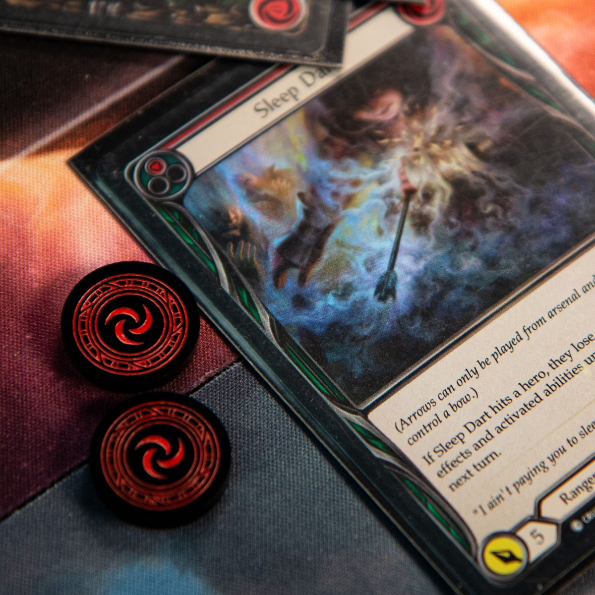 Close up of two Resource Tokens from the Majestic Token Set next to the Flesh and Blood card, Sleep Dart (Red)