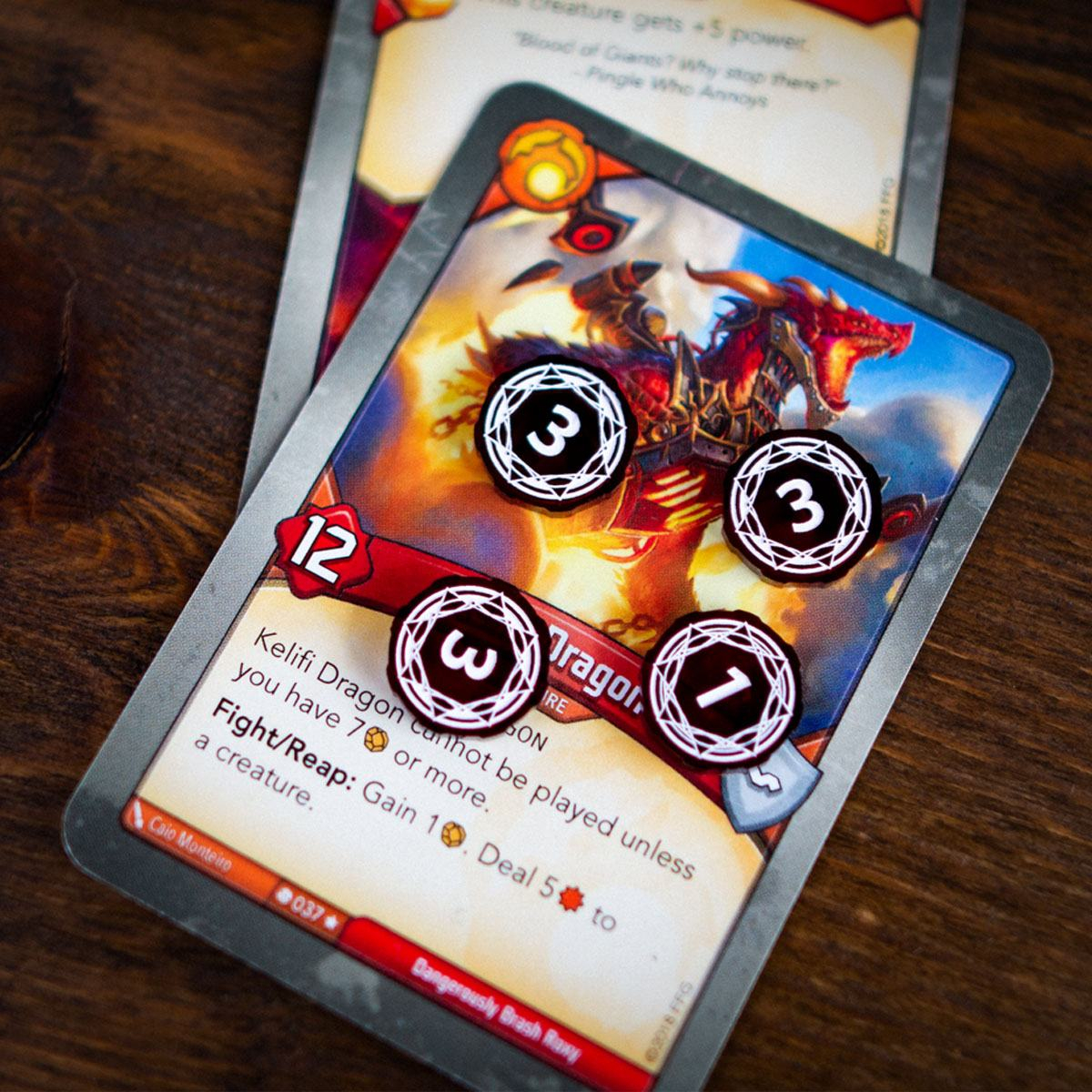Primary Set Damage tokens on the Kelifi Dragon card from Keyforge, three tokens are on their three-damage side and one tokens are on its one-damage side.