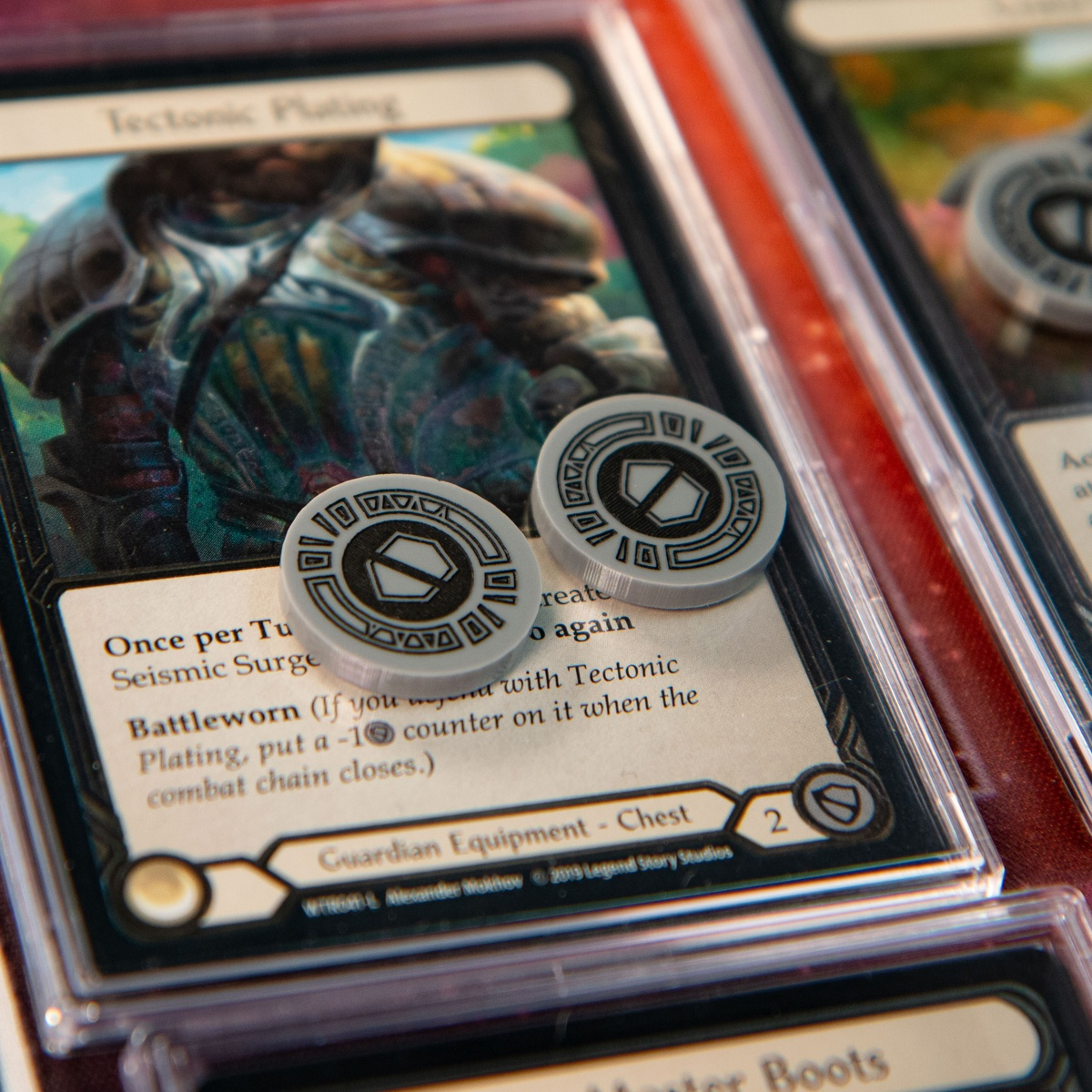 Two Armor Tokens from the Majestic Token Set on the Flesh and Blood TCG card, Tectonic Plating, denoting -2 Armor