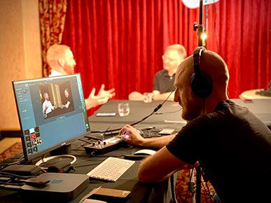 Jonathan sitting at a computer monitoring a video-recorded conversation between Steven and his guest.