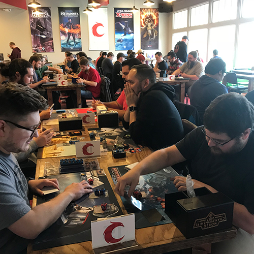 Players sitting at a table at Covenant for a tournament with table markers.